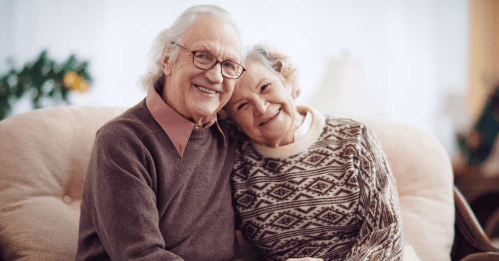 Manželé v důchodovém věku sedí na pohovce a oblímají se.